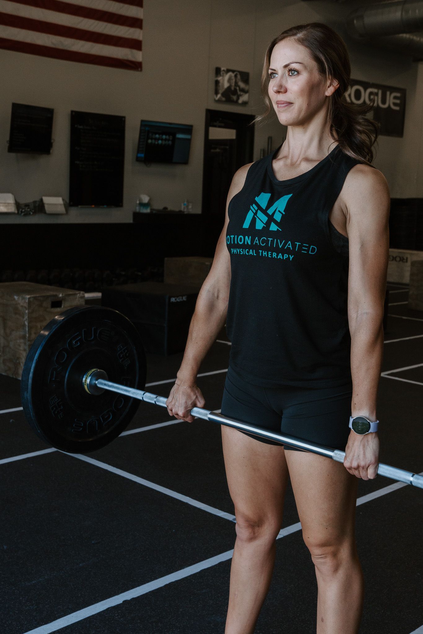 Athlete in black tank top holding a loaded barbell in a gym.