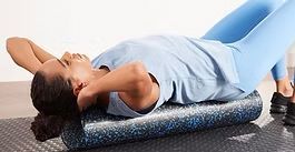 Person lying on a foam roller, stretching their back on a gym floor.
