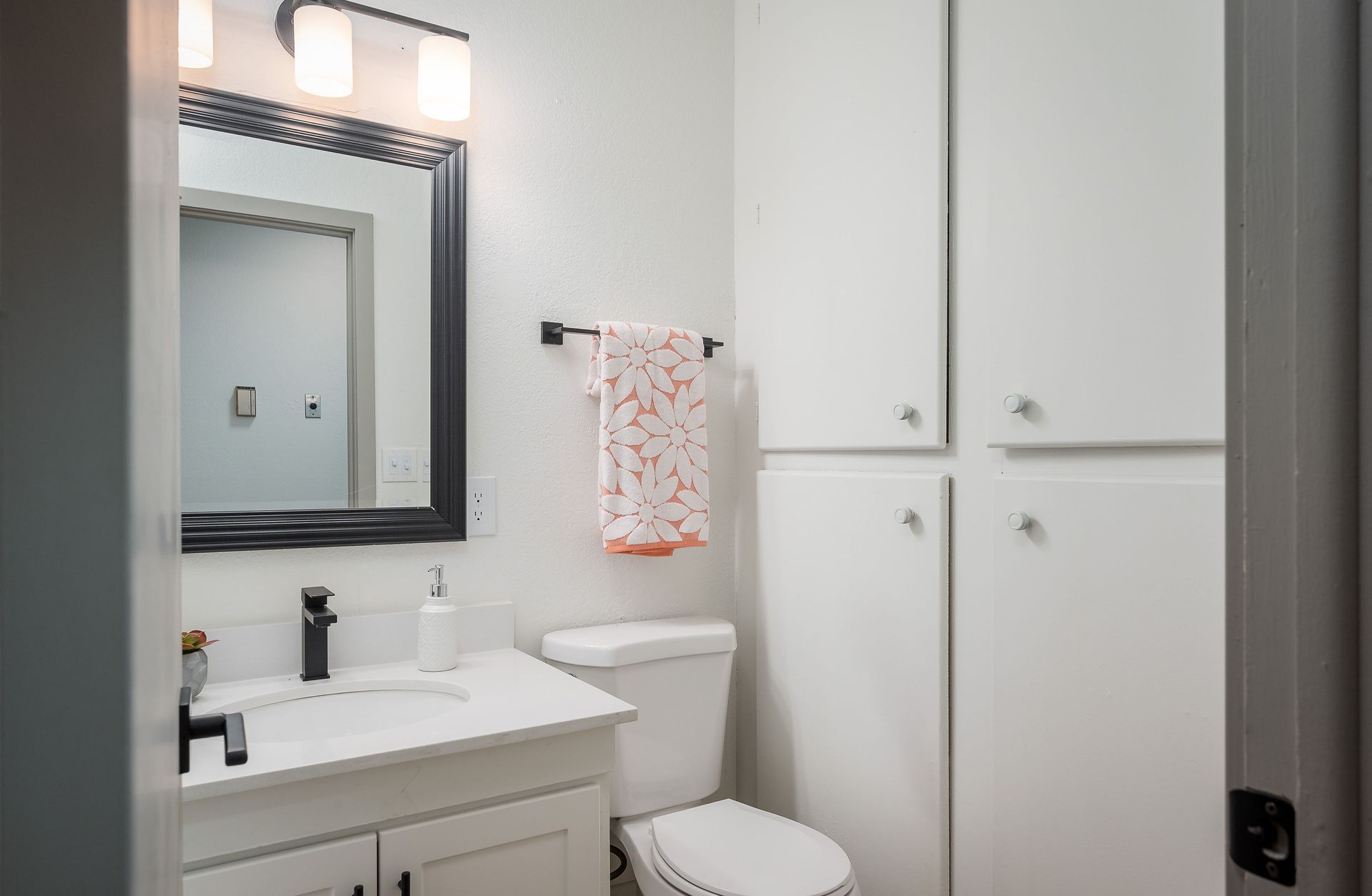Bathroom with white cabinetry, toilet, sink, mirror, and towel rack.