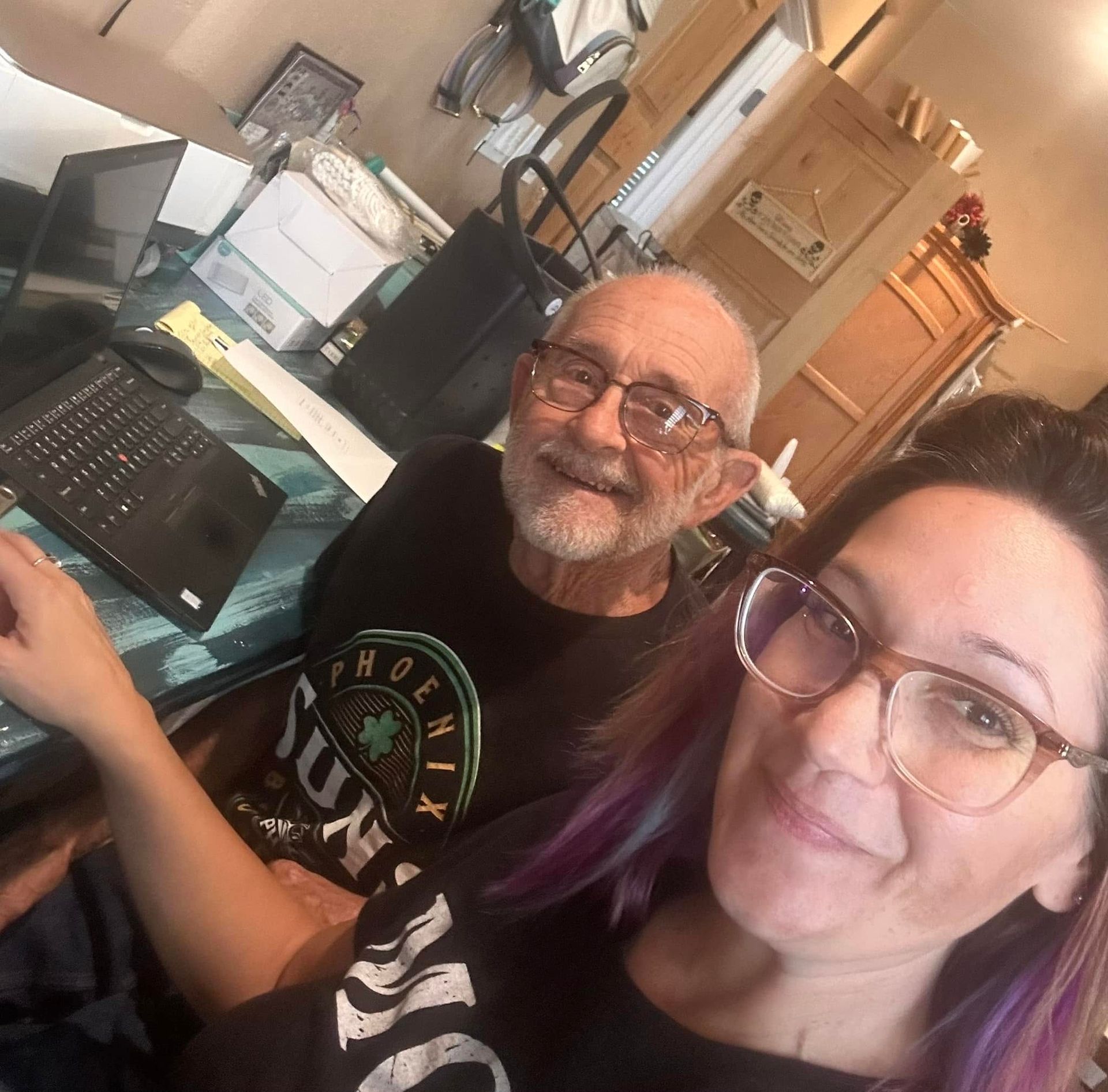 Two people smiling at a desk with a laptop in a home office