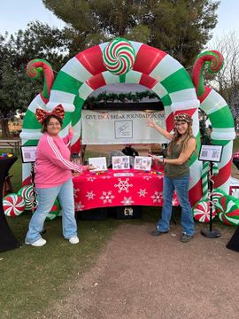 Two people posing beside a red-and-green candy cane holiday booth outdoors