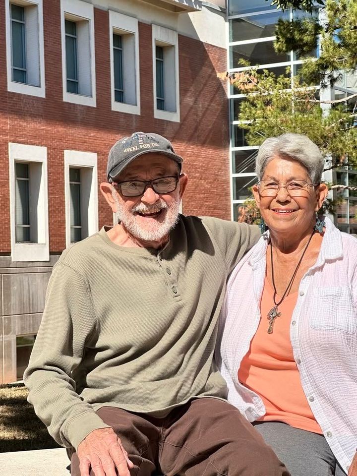 Two smiling adults sitting together outdoors in front of a brick building