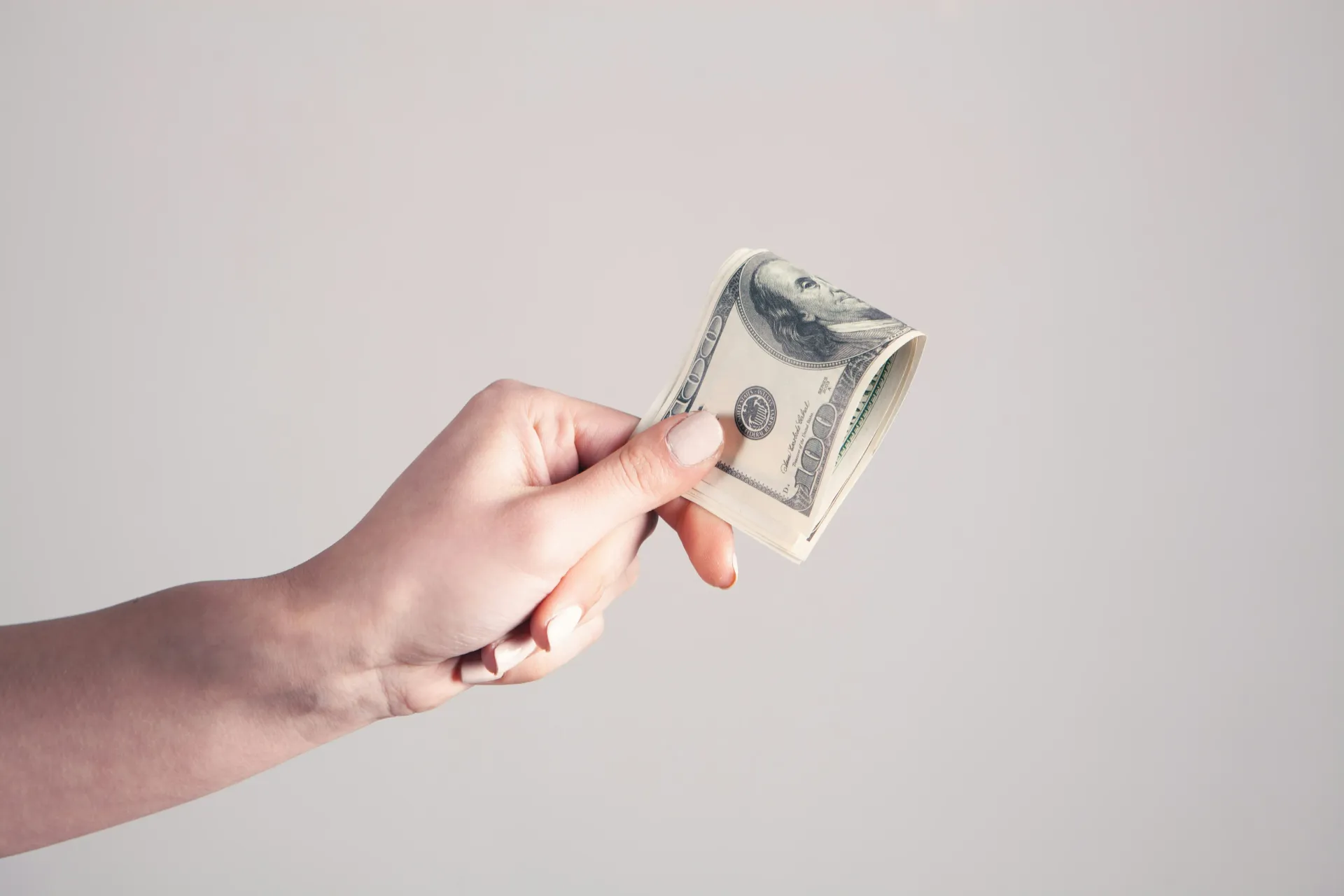Hand holding a small folded dollar bill against a plain light background