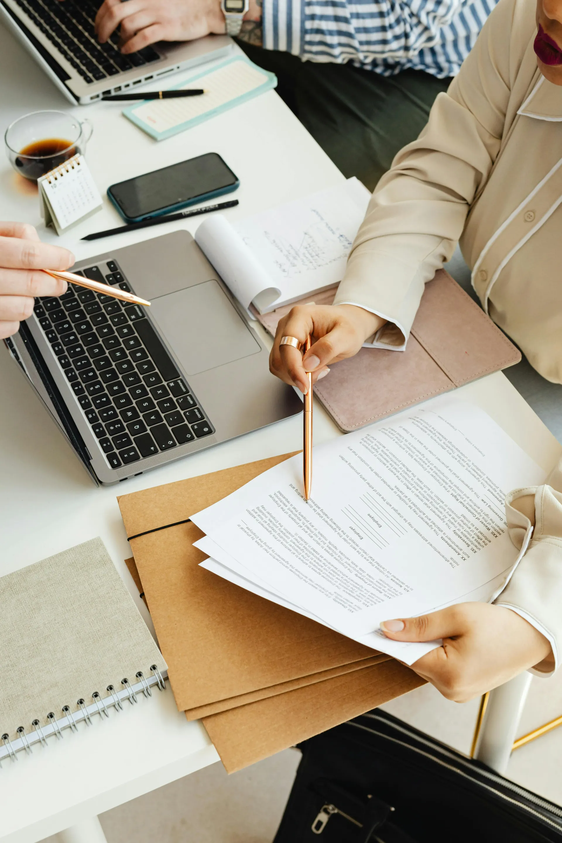 Hands reviewing documents at a desk with laptop, notebook, and coffee cup