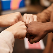Several hands of different skin tones fist-bump together in a close-up group gesture.