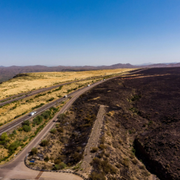 Aerial view of a road beside a dark volcanic lava field and yellow grassland under a clear blue sky