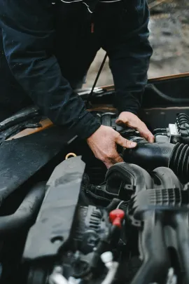 Mechanic working on a car engine, hands adjusting a black air intake in the engine bay.