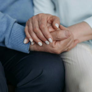 Two people holding hands in a comforting gesture, one in a blue sweater and one in white pants