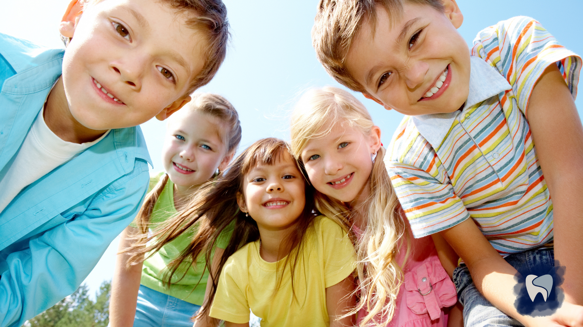 Five children smiling and looking down, with a blue sky background.