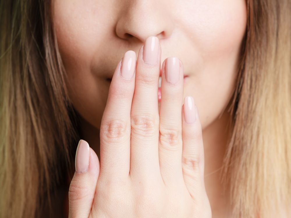 Woman covers her mouth with light-painted nails, with a slight smile and blonde hair.