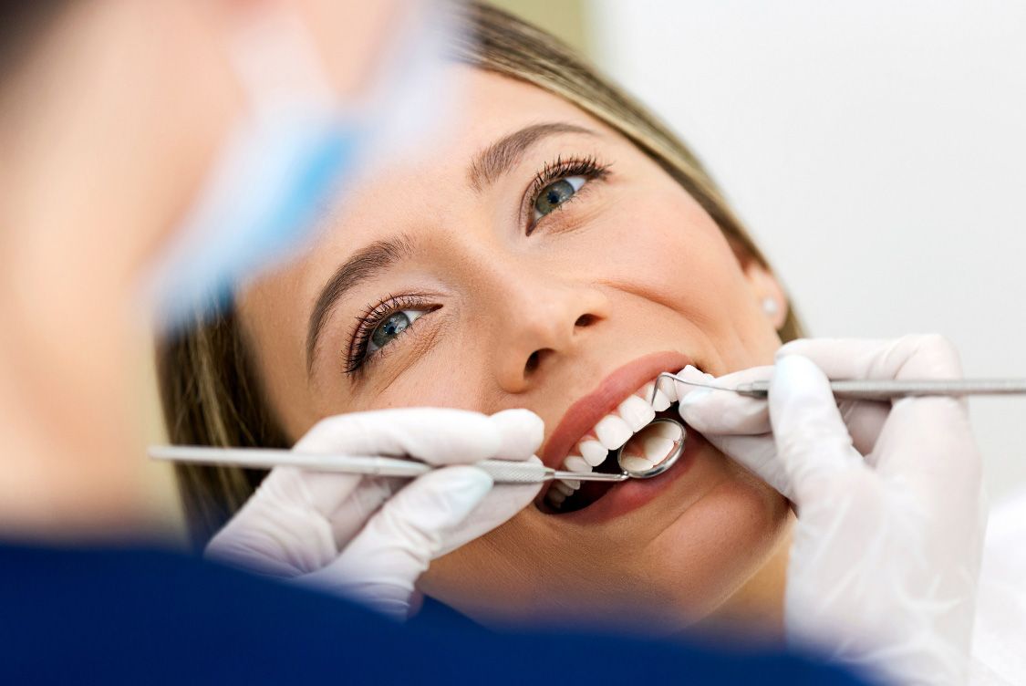 Woman at the dentist's office with mouth open while dentist examines her teeth.