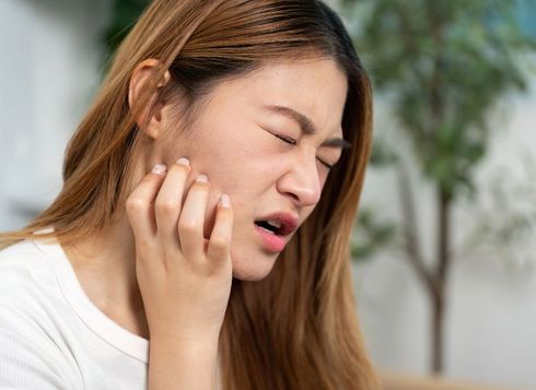 Woman with closed eyes, scratching her cheek, appears to be in pain or discomfort.
