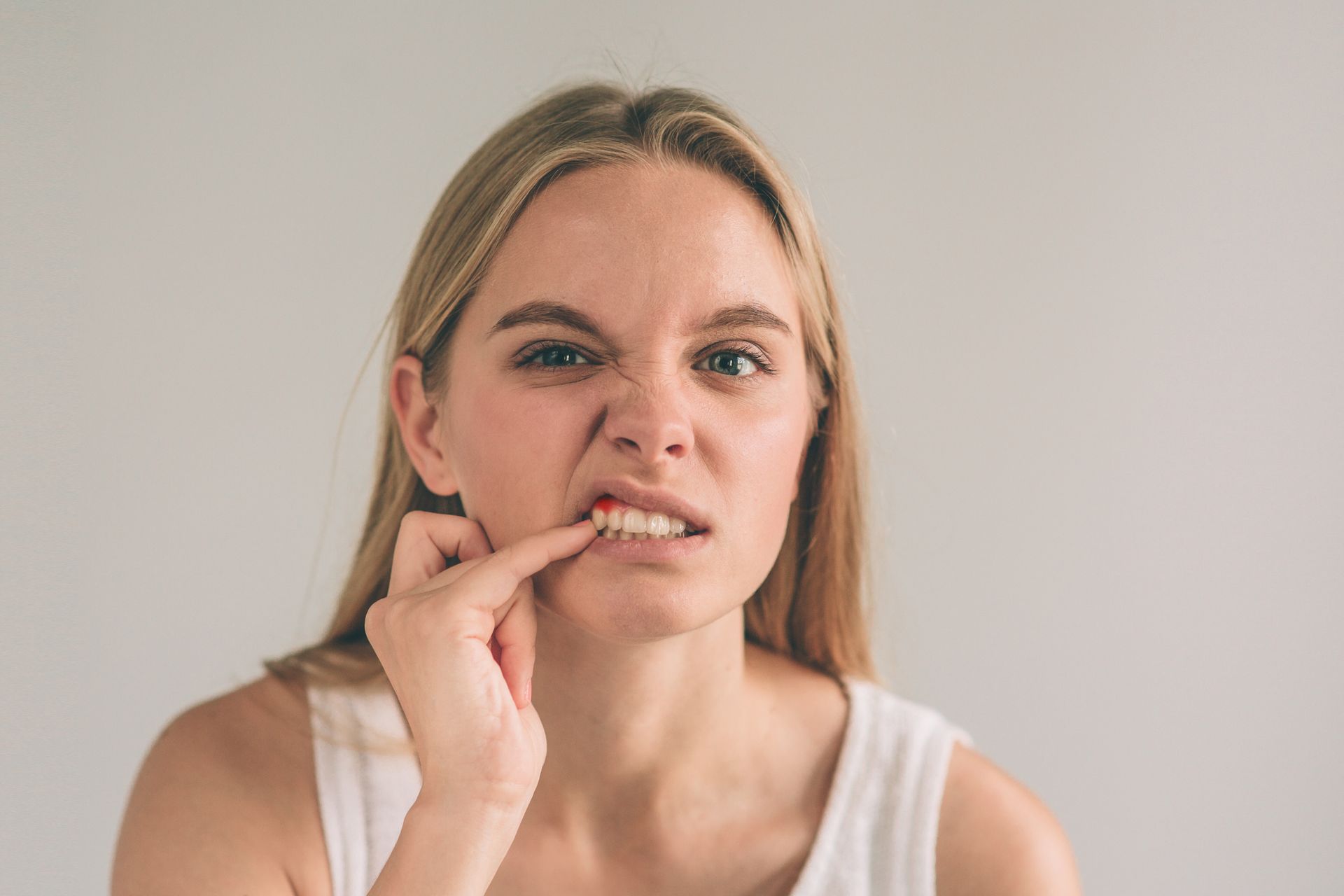 Woman with blonde hair frowning, pointing at her mouth, possibly experiencing tooth or gum discomfort.