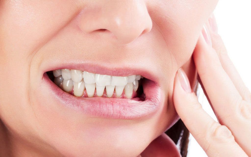 Woman grimacing, hand on cheek, showing teeth, possible toothache.