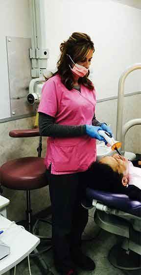 A woman wearing glasses and a pink shirt is looking at the camera.
