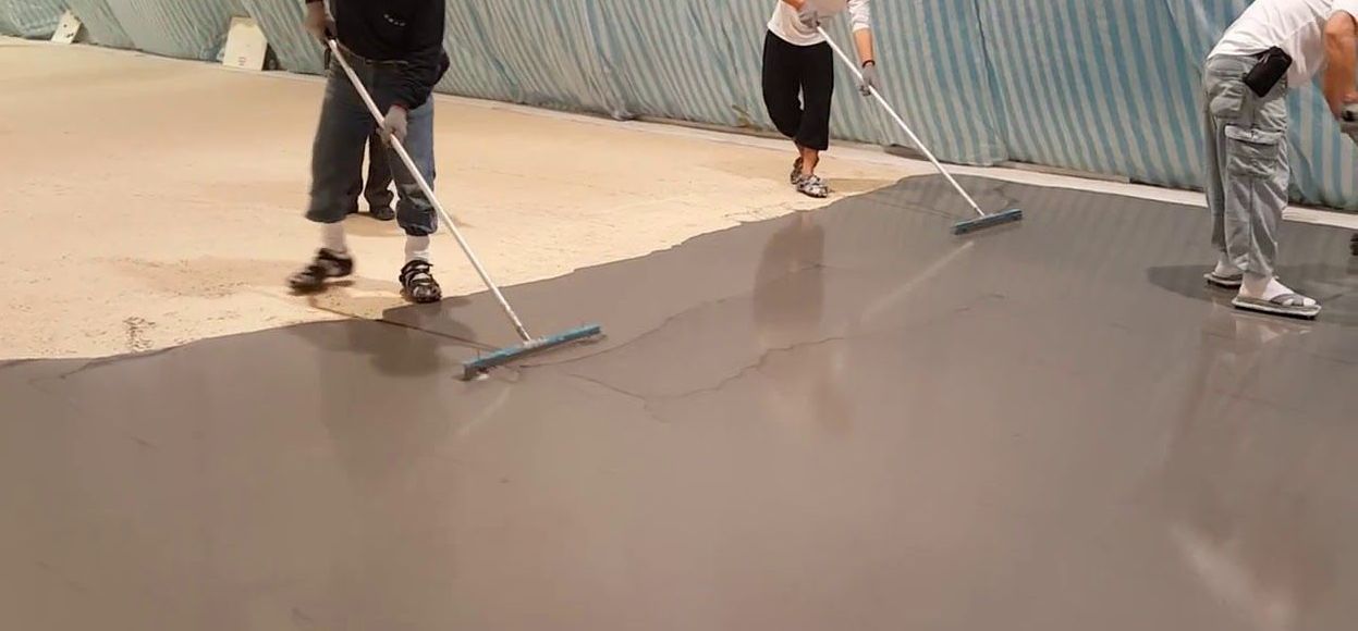 Workers smoothing wet concrete on a sloped surface with squeegees and tools.