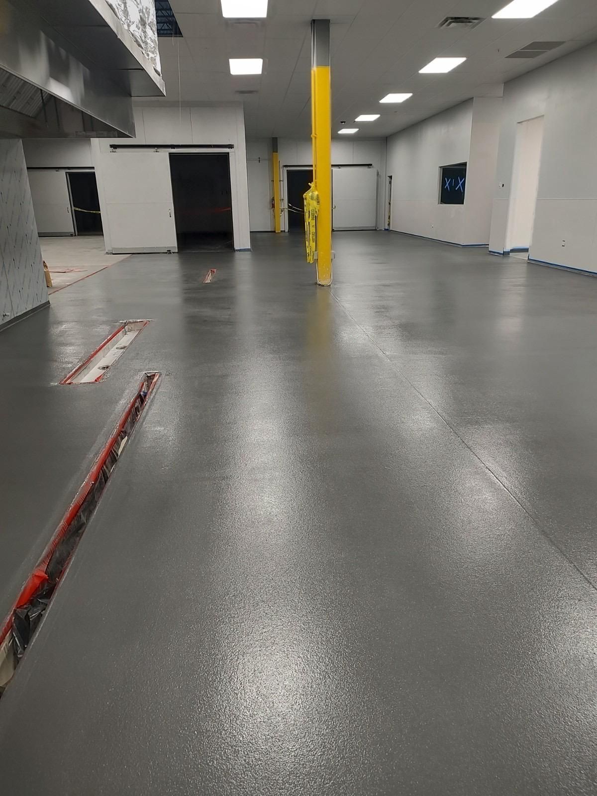 Empty indoor warehouse with gray floor, white walls, and a bright yellow support column.