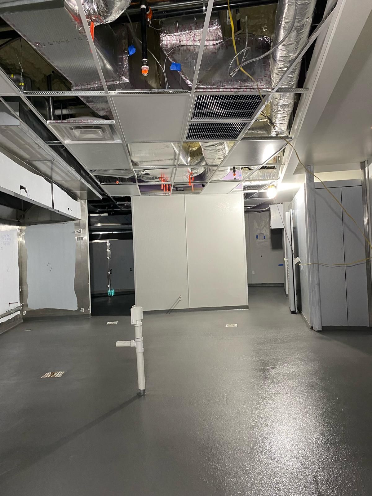 Empty industrial basement with exposed ceiling, white panels, and wet concrete floor.