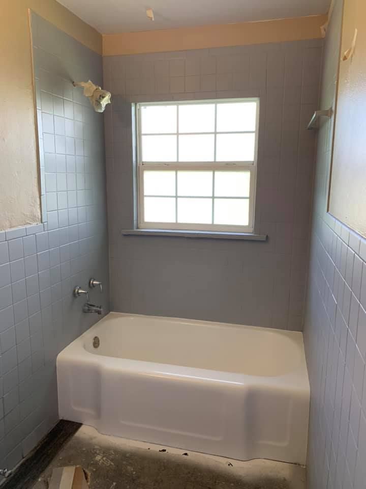 Bathroom with white tub, light blue tiles, and a window with white trim.