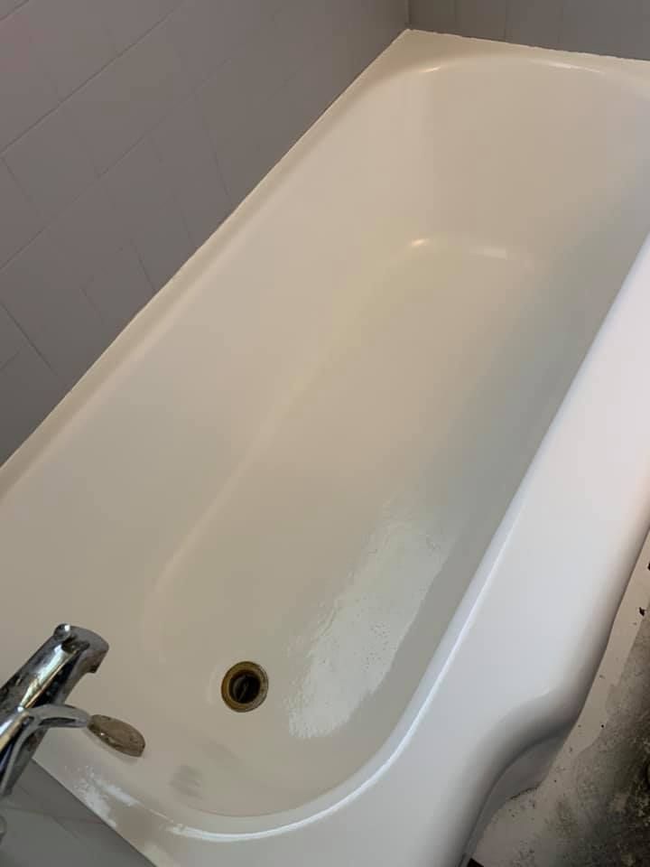 White bathtub with faucet and drain, set against gray tiles.