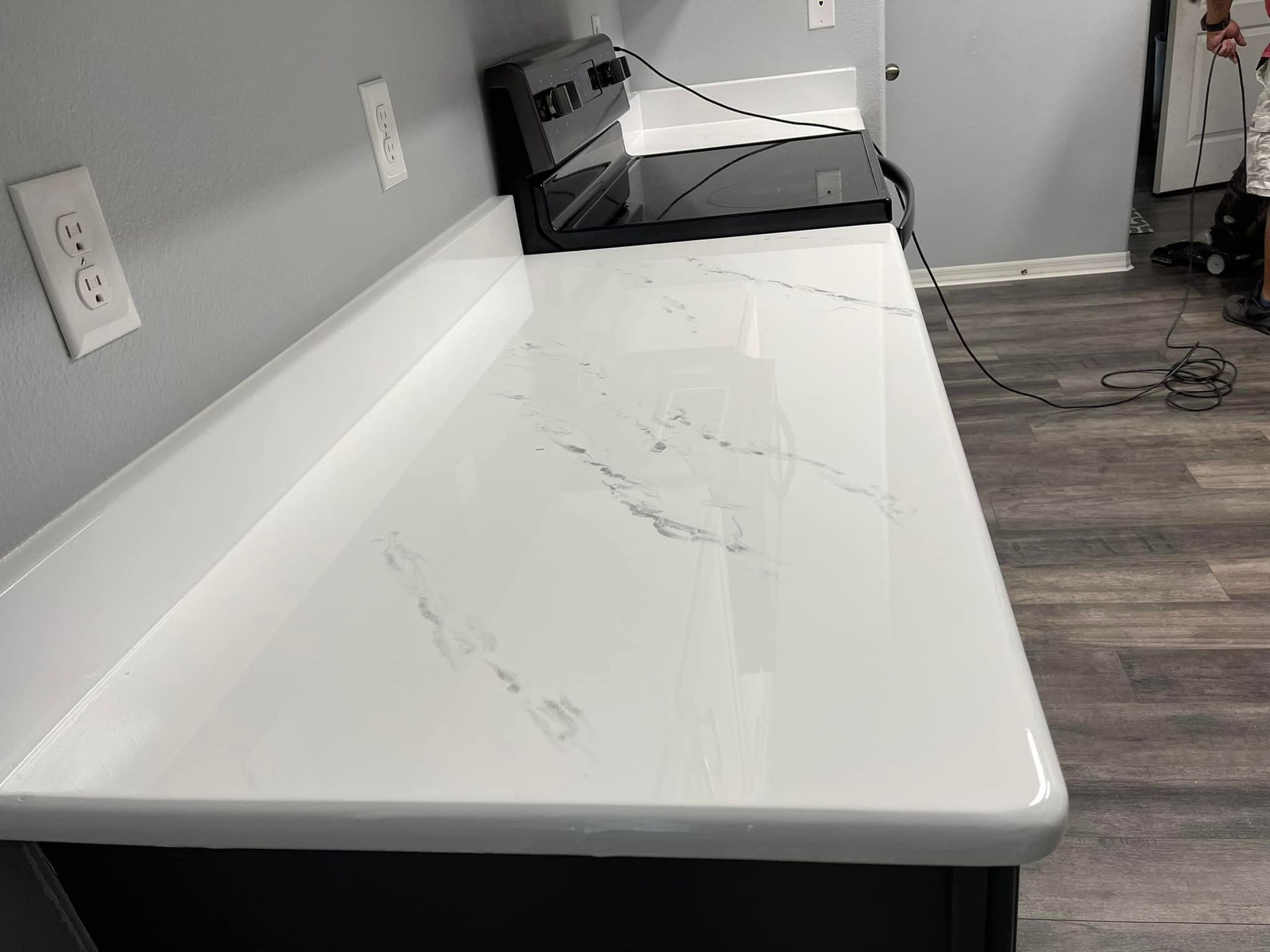 White countertop with grey veining, mounted to black cabinets against a grey wall.