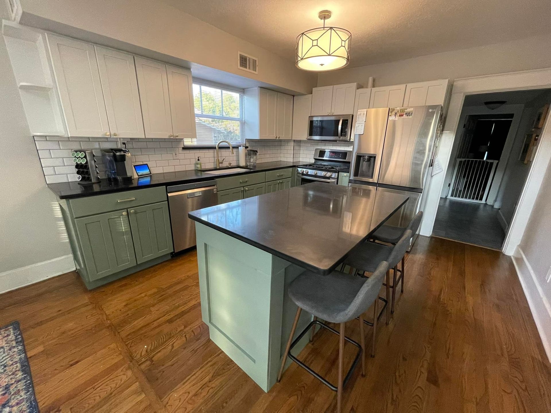 Modern kitchen with green cabinets, stainless steel appliances, and a gray countertop island.