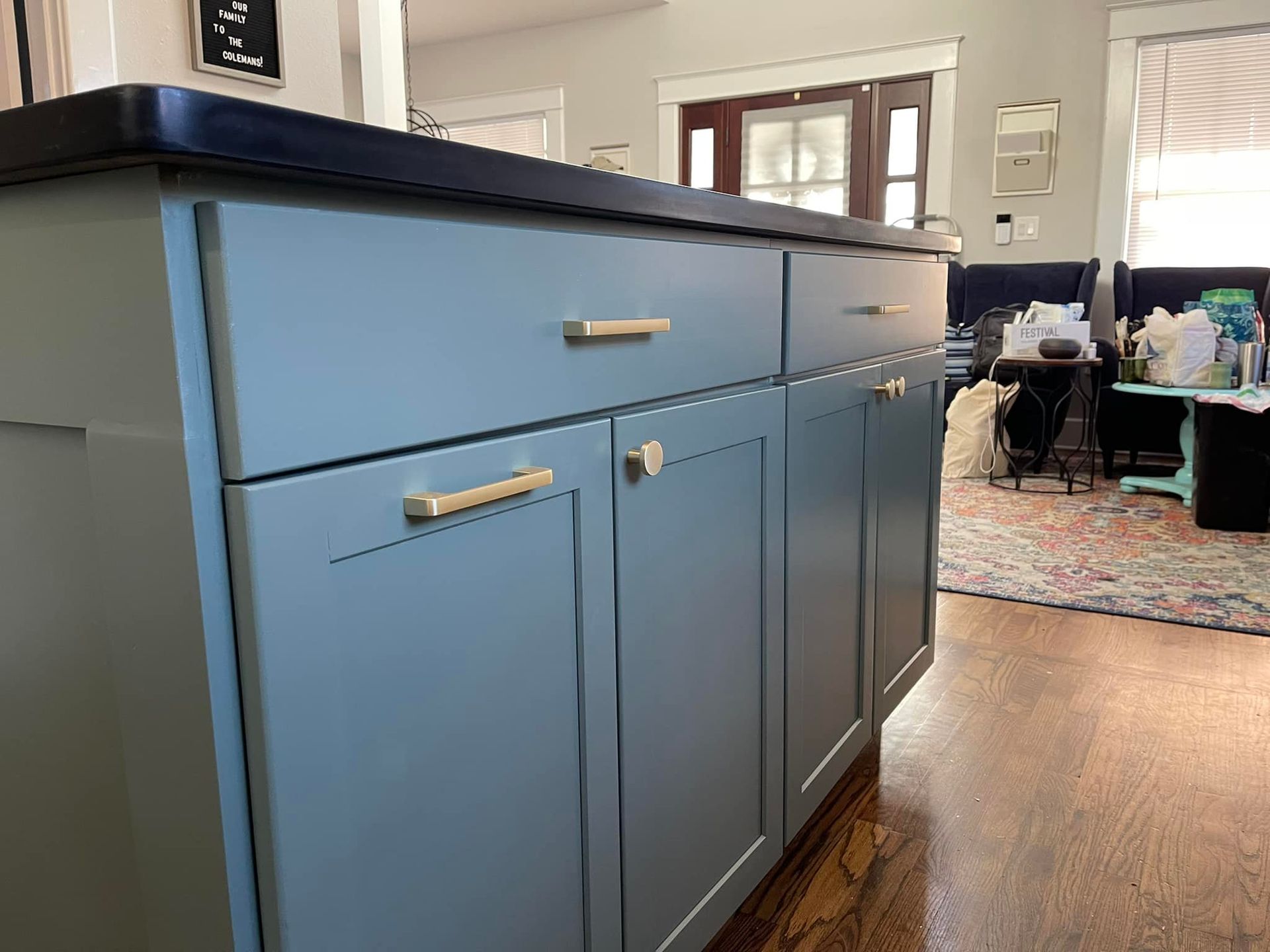 Blue kitchen cabinets with gold hardware and black countertop.