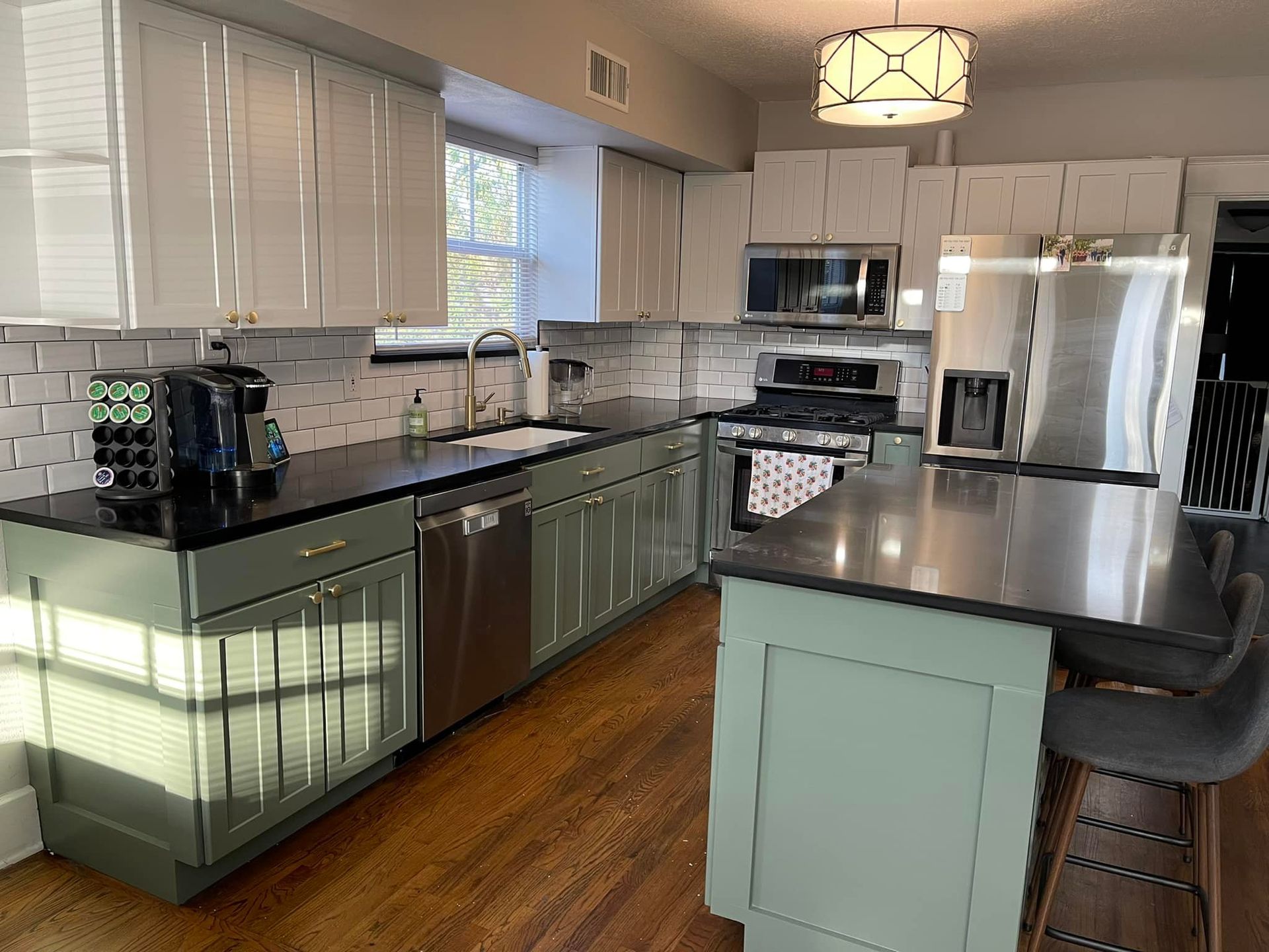 Modern kitchen with green and white cabinets, stainless steel appliances, and a black countertop.