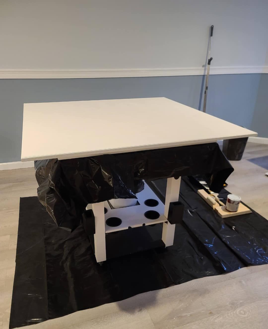 A white square table covered in black plastic, set up for painting in a room.