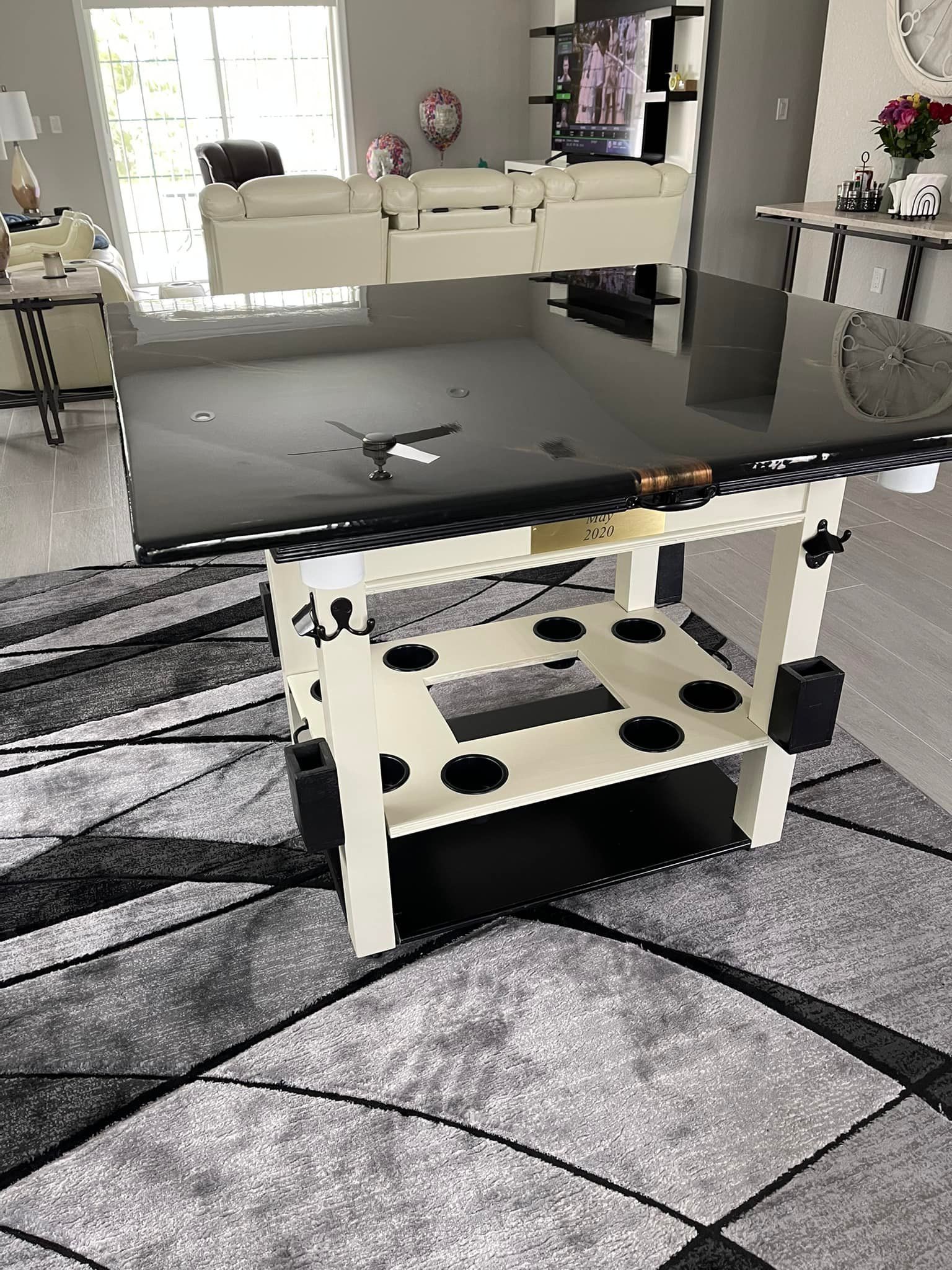 Pool table with black top, white frame, and accessories on a patterned rug.