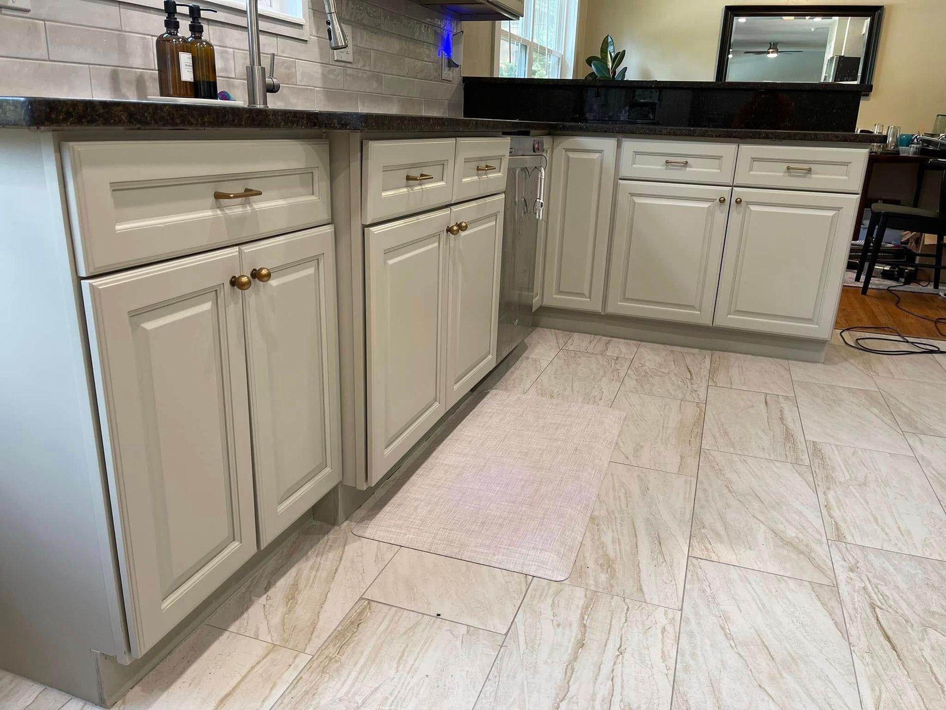 Cream-colored kitchen cabinets with gold hardware, dark countertops, and tile flooring.