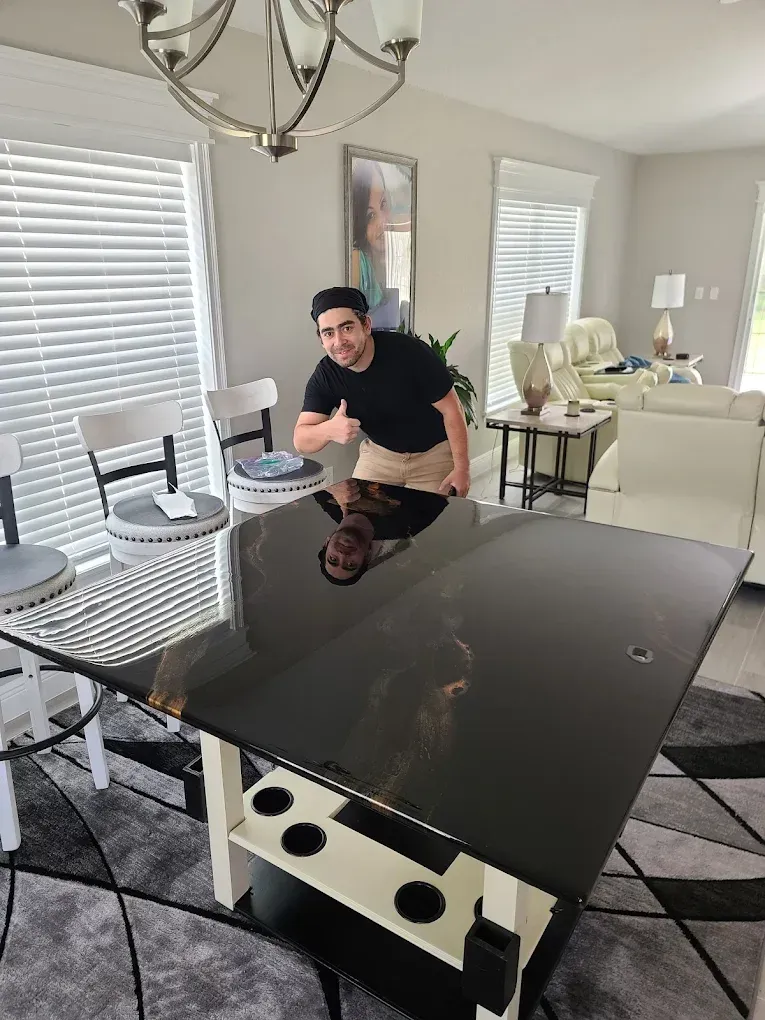 Man giving thumbs up next to a black glossy table with built-in cup holders in a bright living room.