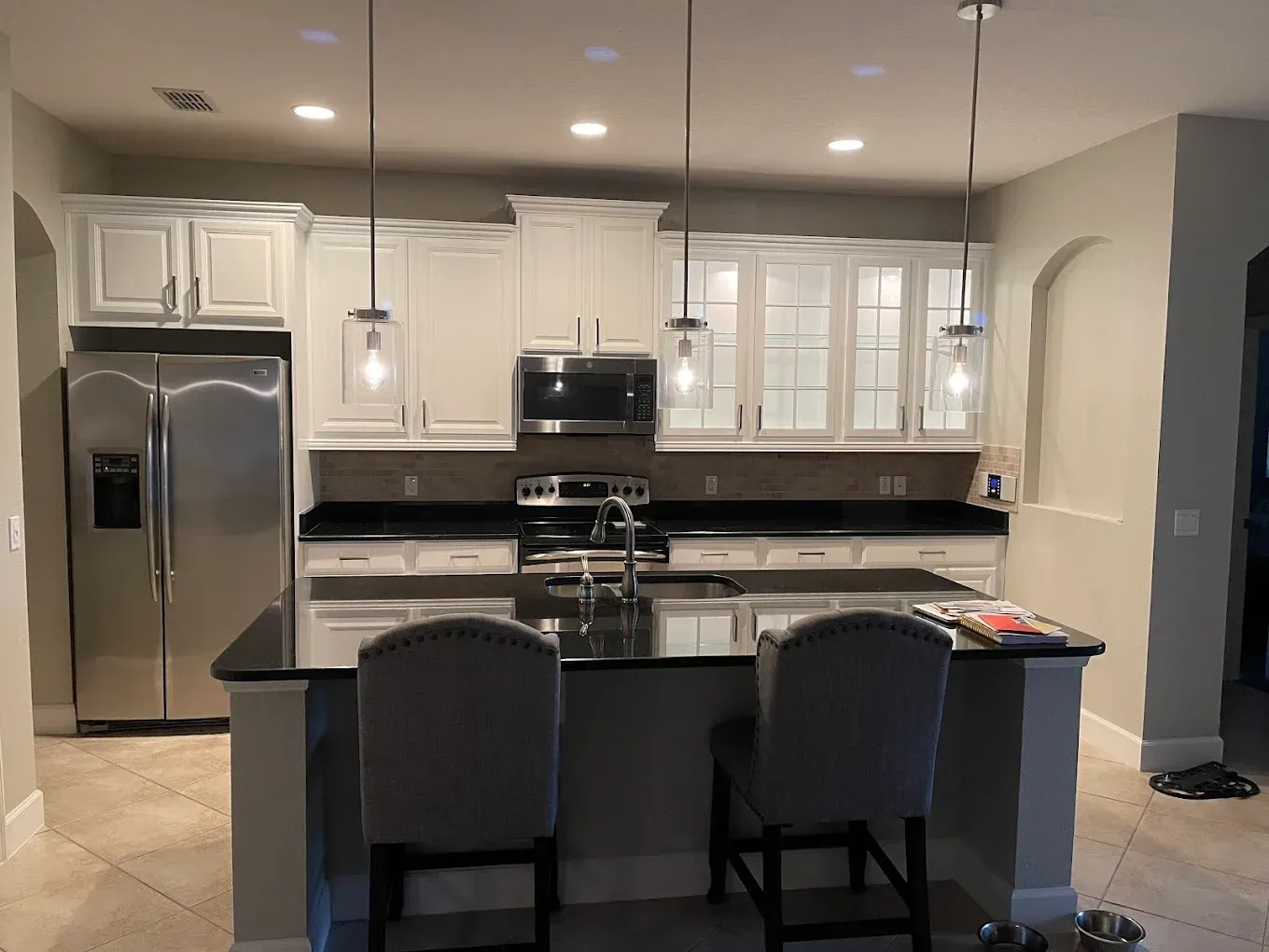 White kitchen with black countertops and island, stainless steel appliances, and three pendant lights.