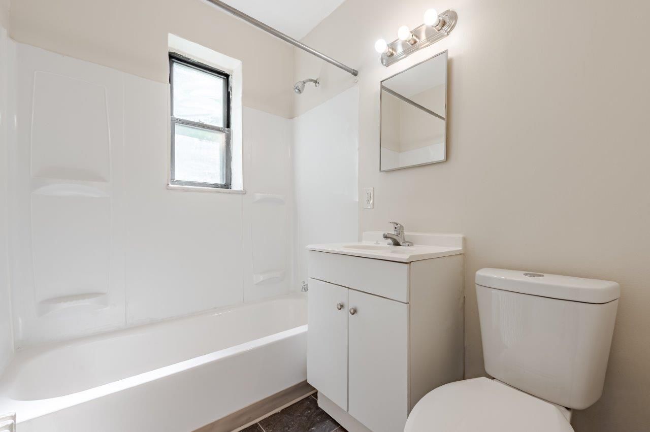 Bright white bathroom with tub, toilet, sink vanity, mirror, and small window