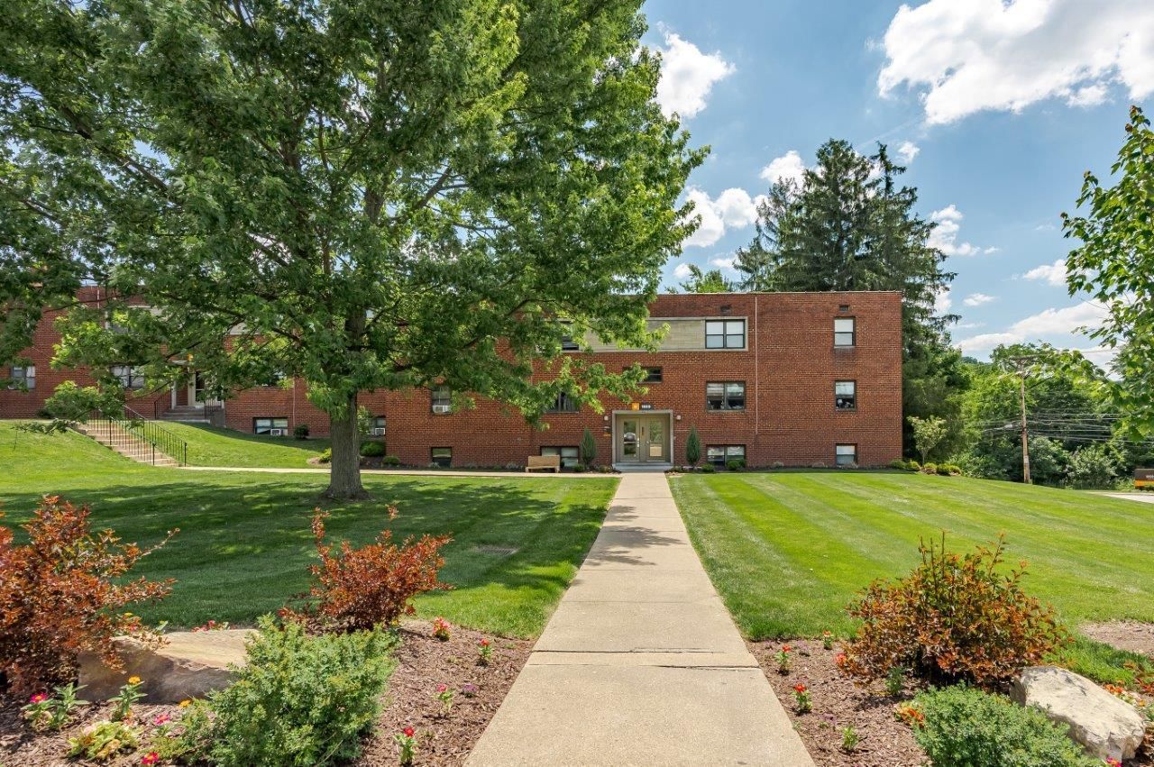 Brick apartment building with a central walkway, green lawn, and trees under a blue sky