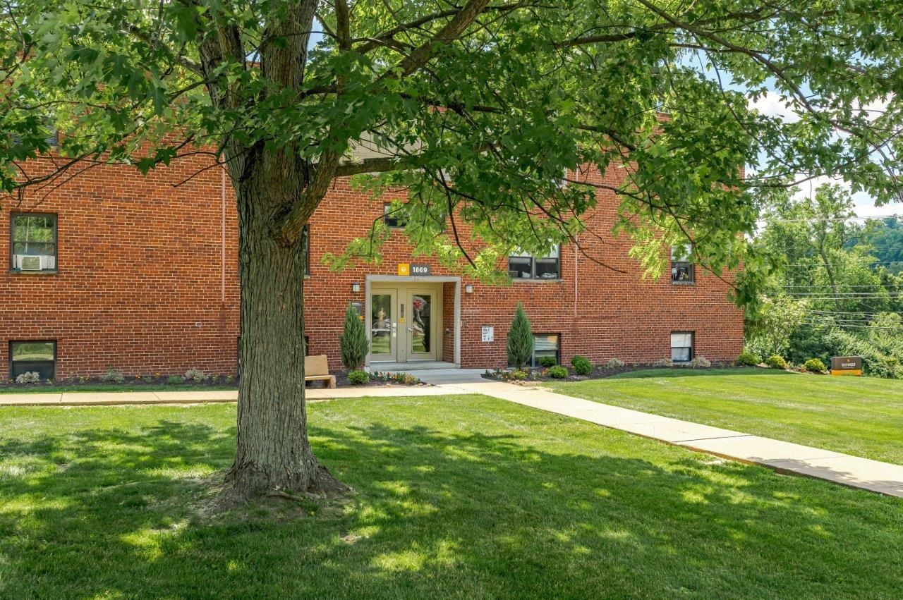 Brick apartment building with a tree-lined lawn and sidewalk leading to the entrance