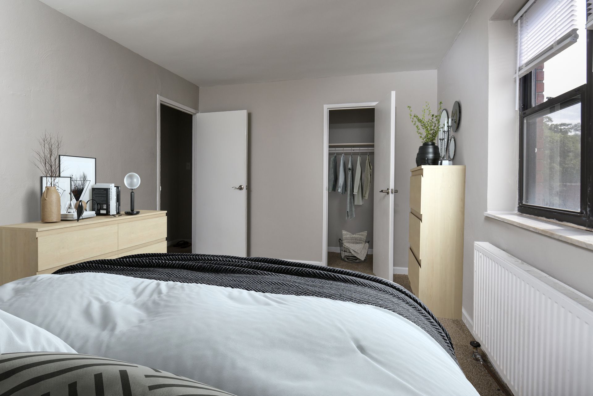 Bedroom with a bed, dresser, closet, and window. Light gray walls and light wood furniture.
