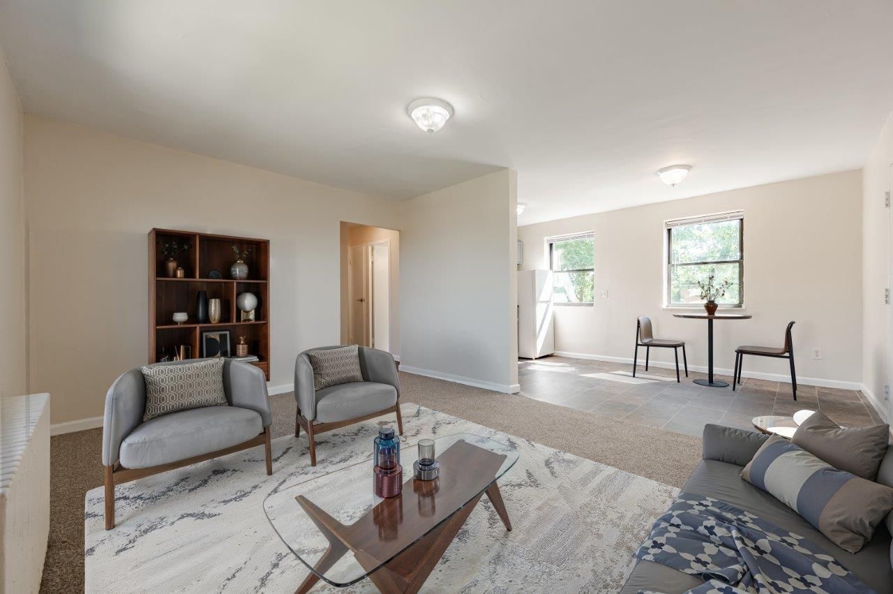 Bright living room with gray sofas, coffee table, and a bookshelf near windows and a dining area.