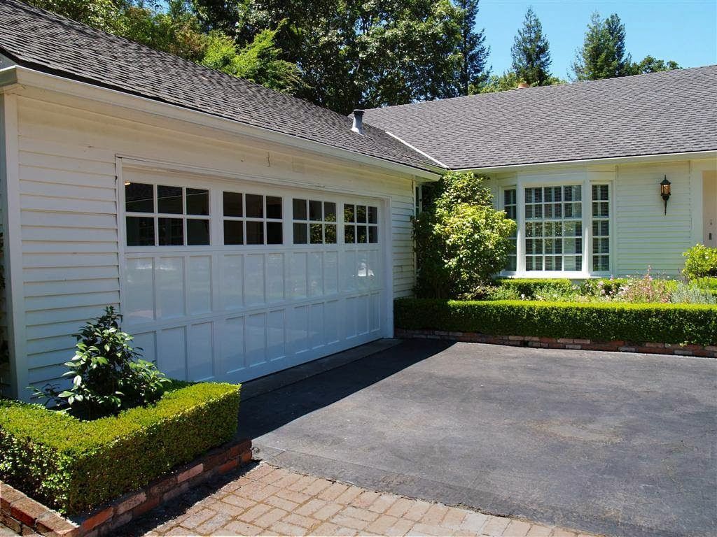 Suburban house driveway with white garage, brick accents, and manicured hedges under a sunny sky
