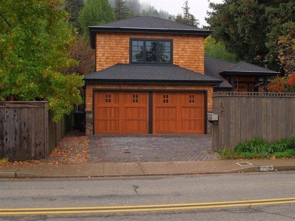 Two-story house with wood siding, double garage, and fenced front yard on a tree-lined street