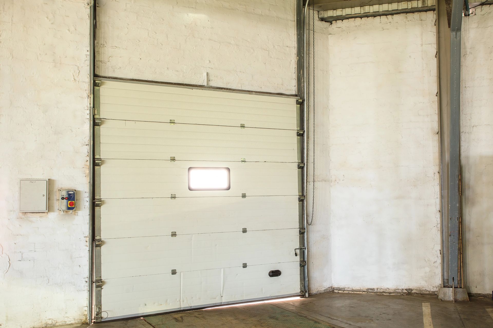 Industrial warehouse interior with a large white garage door and a small window panel