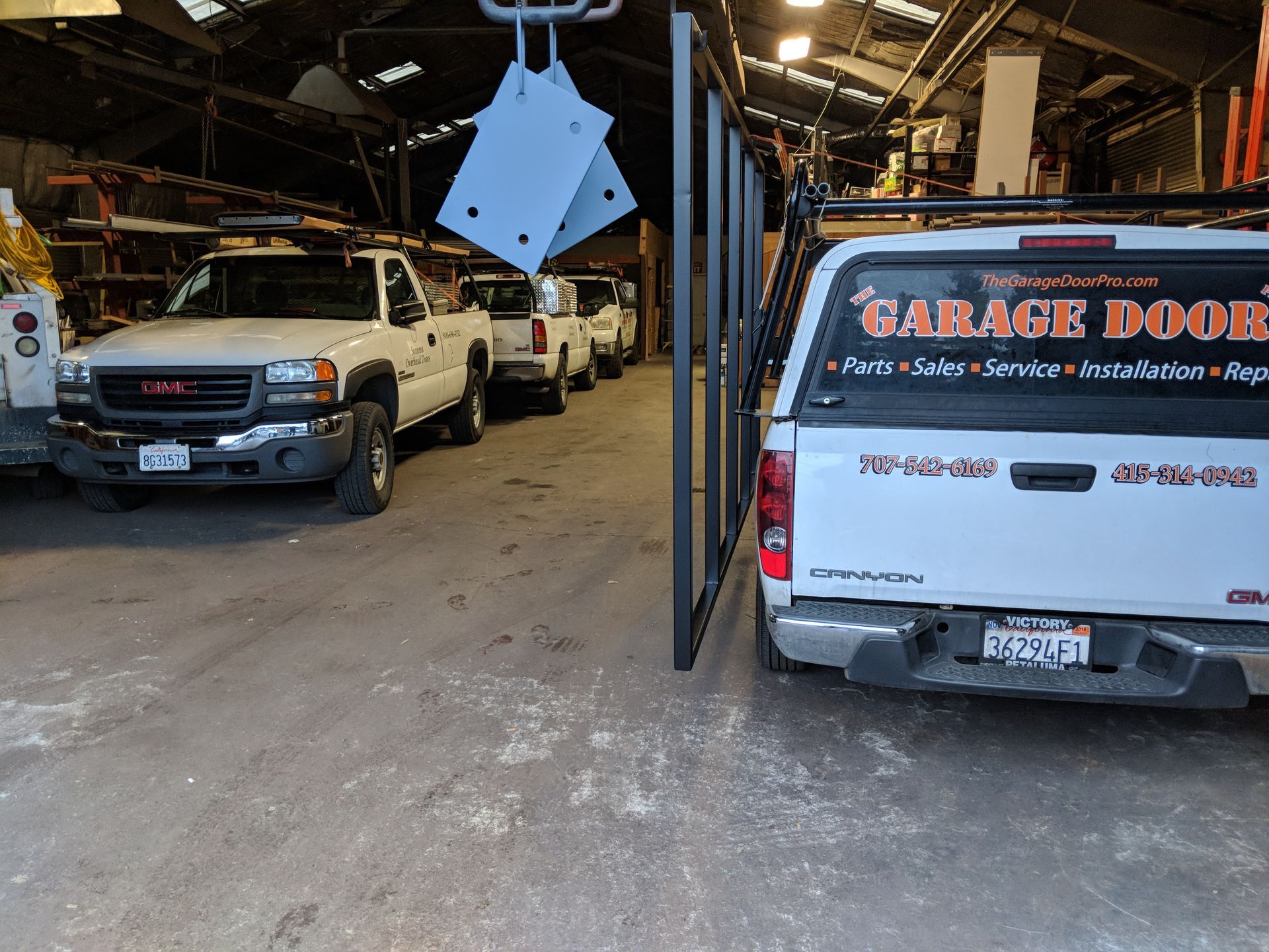 Indoor auto shop with white work vans lined up under a hanging blue panel