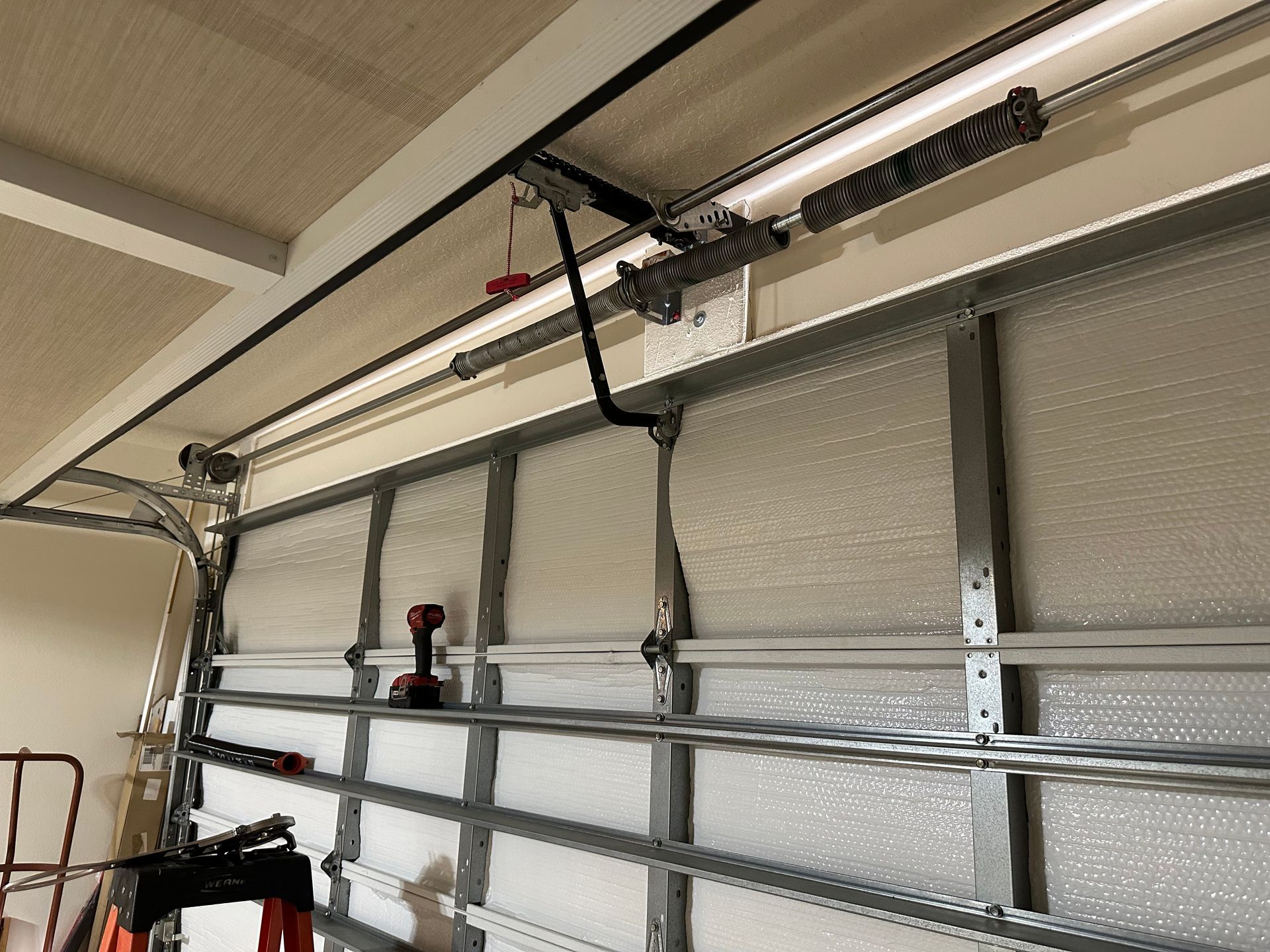 Garage door with metal reinforcement bars and overhead opener rails mounted near the ceiling.