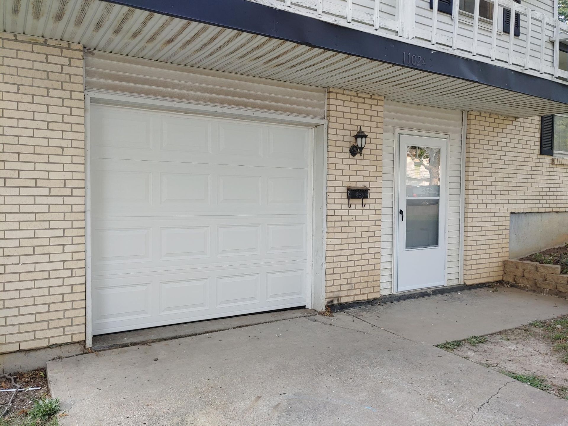 White garage door and front entry on a beige brick townhouse exterior.