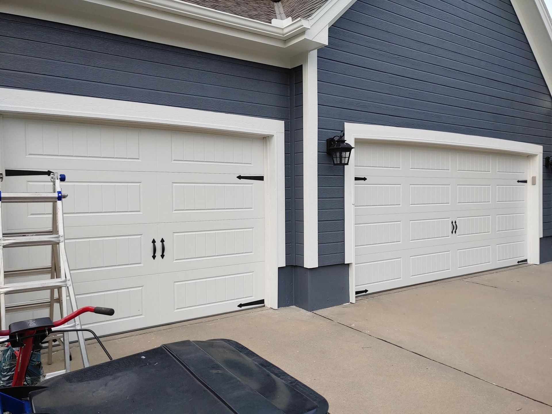 Two white garage doors on a blue house exterior, with a driveway in front.