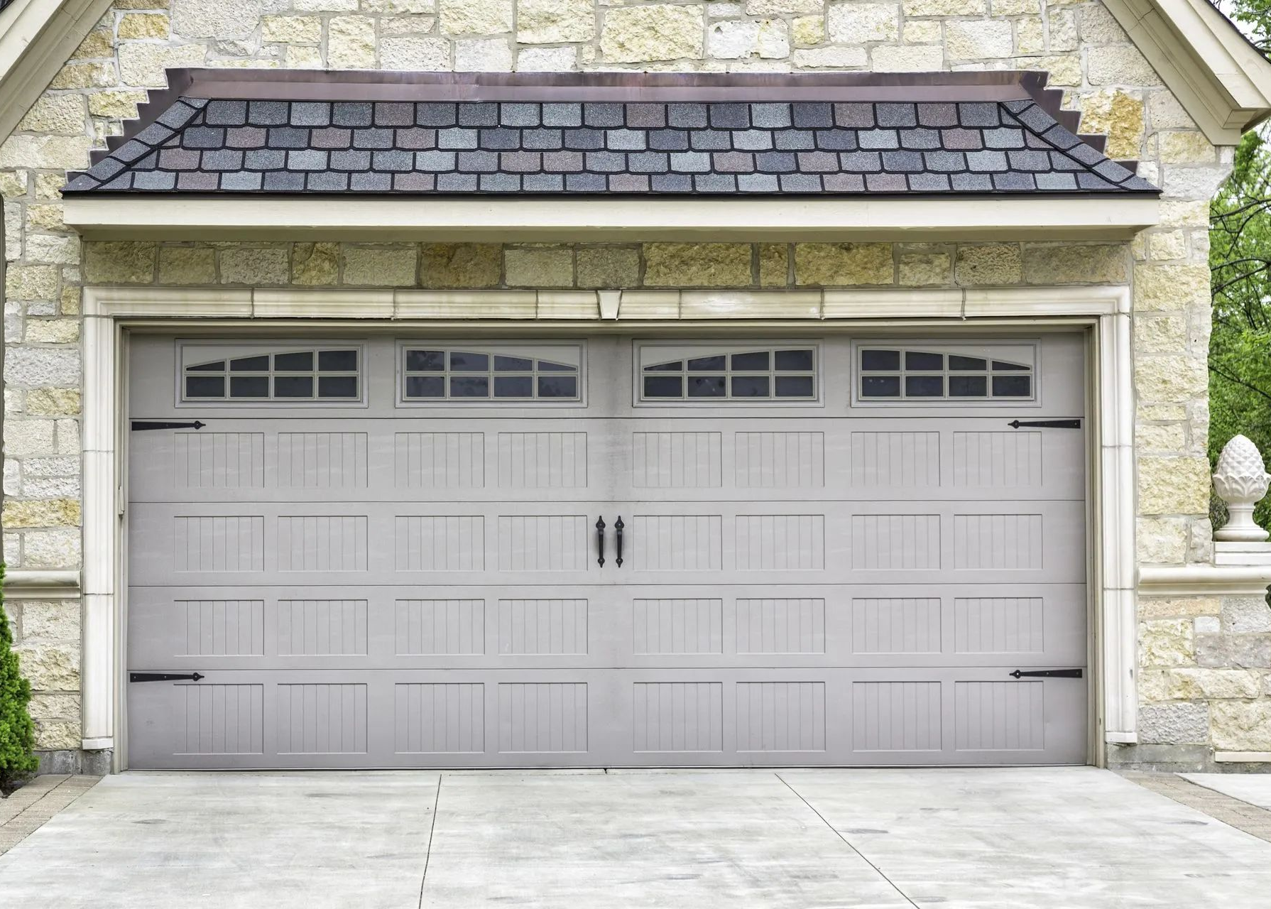 Gray double garage door on a stone house exterior with small windows above and a paved driveway