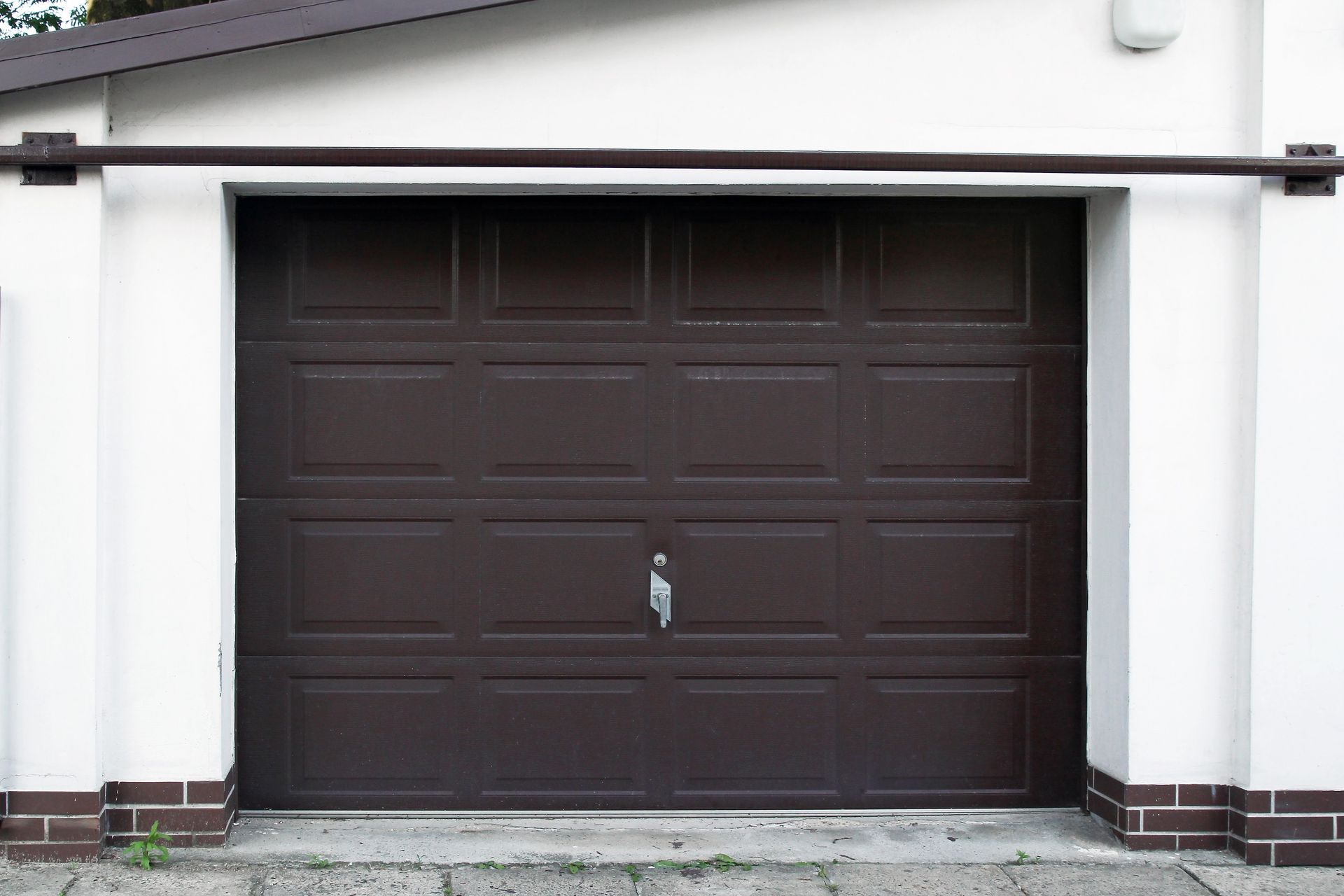 Dark brown garage door on a white house exterior with a small handle centered near the bottom.