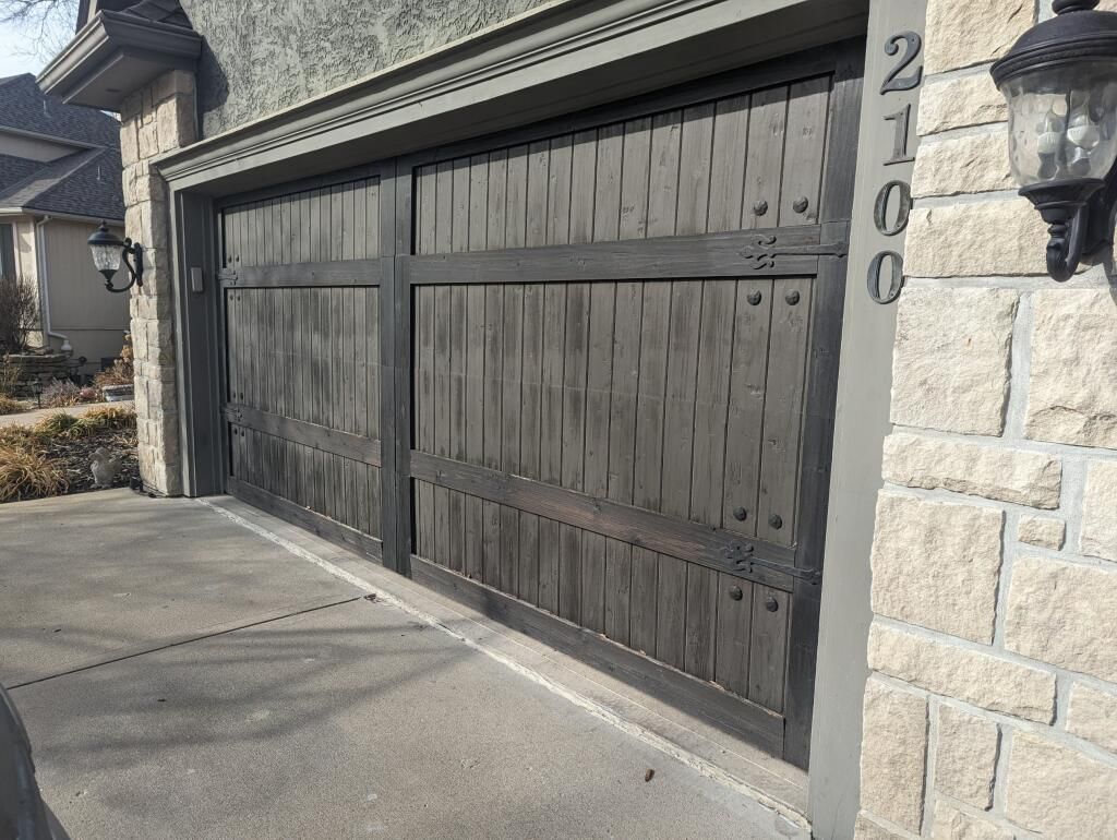 Two-car garage with dark wood doors and stone exterior beside a driveway.