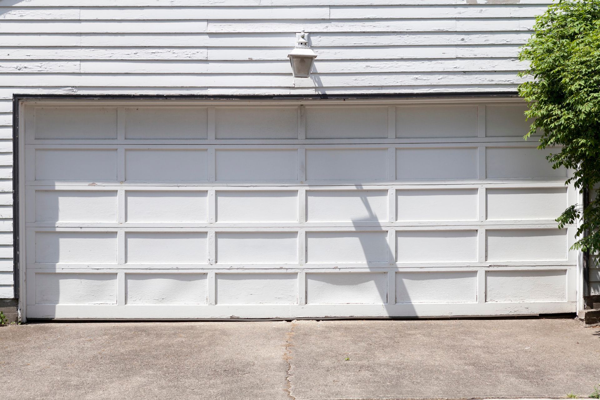 White double garage door on a house with light siding and a concrete driveway.