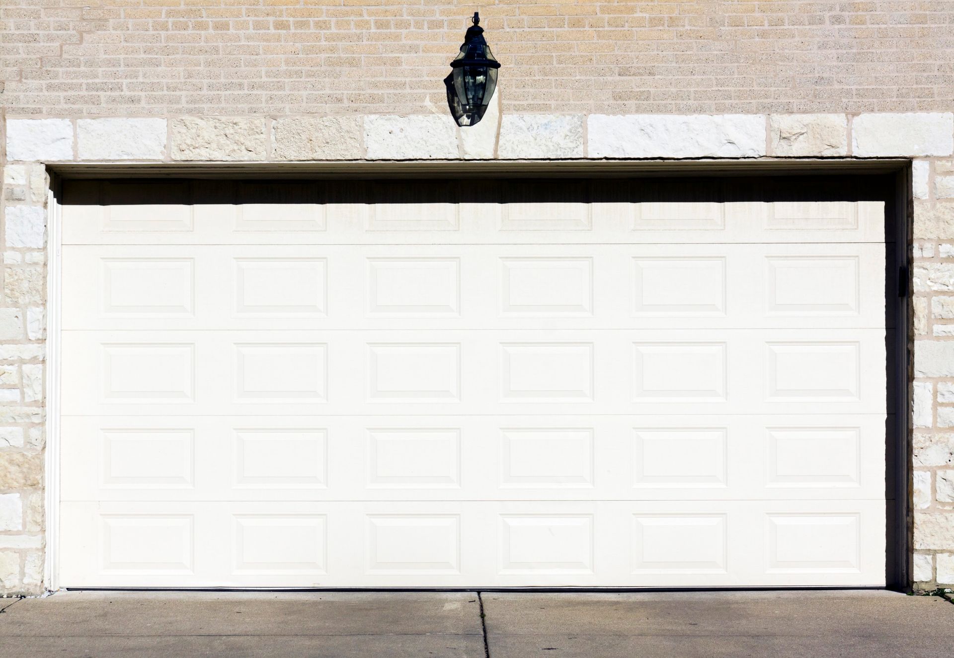 White garage door beneath a brick wall with a black lantern above it